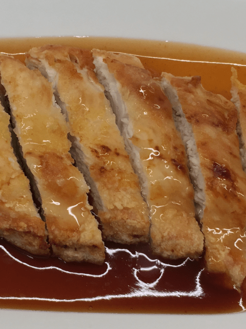 Crispy Chinese takeaway style lemon chicken on a serving plate with sweet & sour sauce.