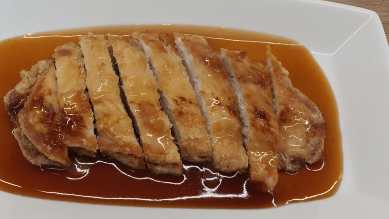 Crispy Chinese takeaway style lemon chicken on a serving plate with sweet & sour sauce.