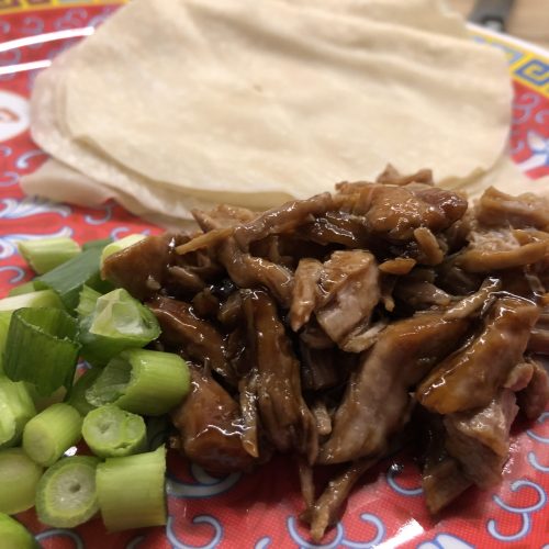 Chinese takeaway style shredded aromatic pork on a serving plate with Chinese pancakes, spring onion and cucumber.