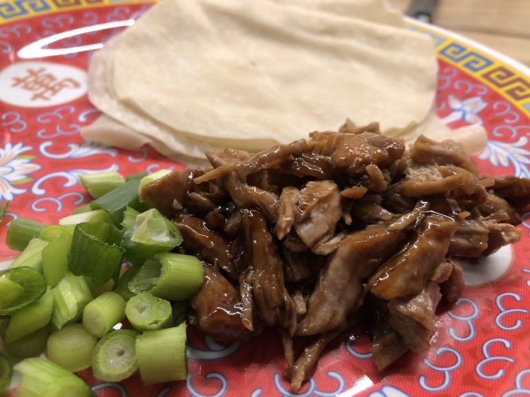 Chinese takeaway style shredded aromatic pork on a serving plate with Chinese pancakes, spring onion and cucumber.