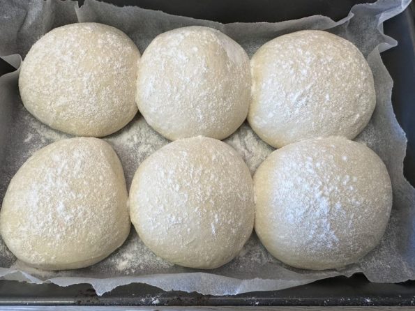 Dough divided and resting on top of greaseproof paper in an oven tray.
