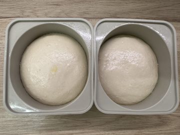 Two prepared pizza dough balls in proofing trays.