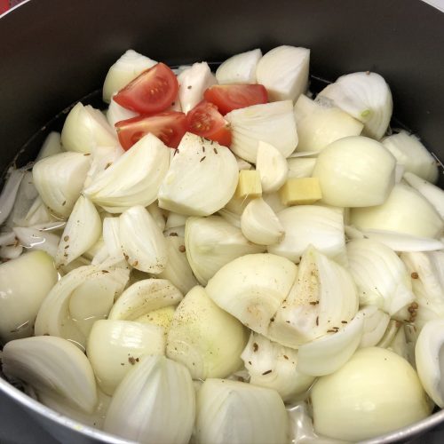 A large stock pot filled with onions and other curry broth ingredients.