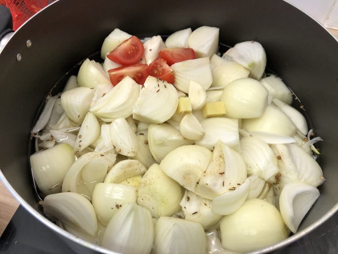 A large stock pot filled with onions and other curry broth ingredients.