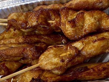 Cooked chicken satay skewers in a Chinese takeaway style foil tray.