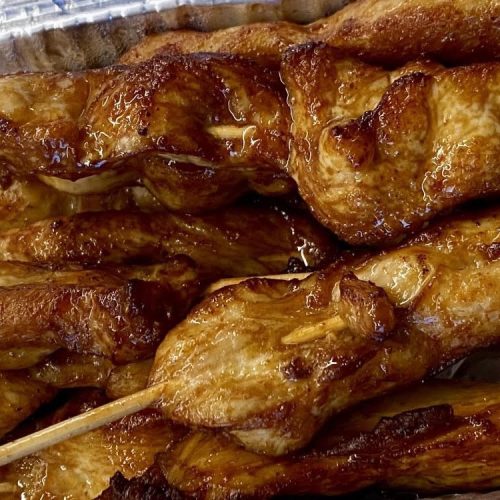 Cooked chicken satay skewers in a Chinese takeaway style foil tray.