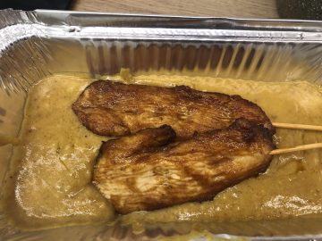 Chinese takeaway style chicken satay skewers in a foil tray with satay sauce.