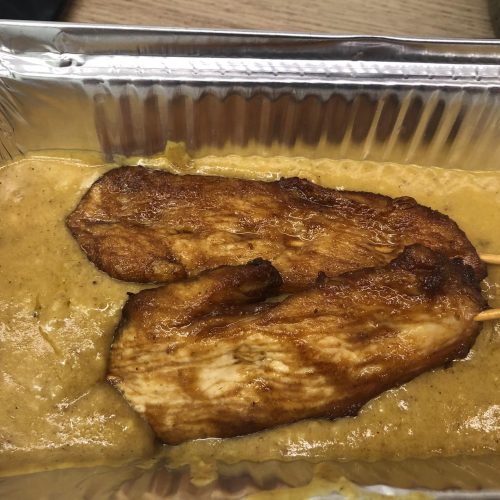 Chinese takeaway style chicken satay skewers in a foil tray with satay sauce.