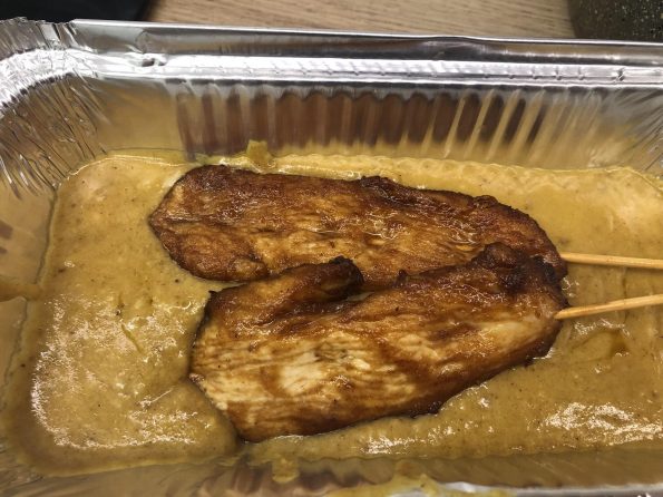 Chinese takeaway style chicken satay skewers in a foil tray with satay sauce.