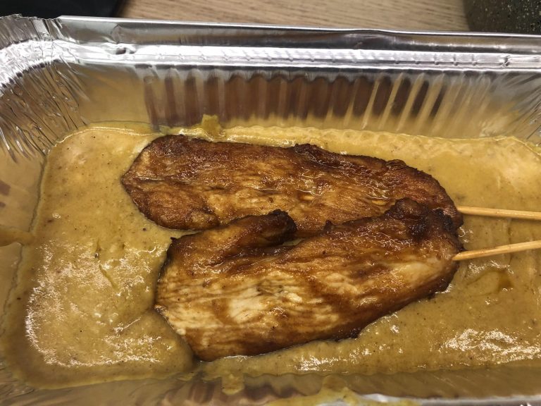 Chinese takeaway style chicken satay skewers in a foil tray with satay sauce.