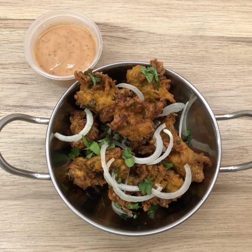 A serving bowl filled with vegetable pakora, beside a dipping pot of pink pakora sauce.