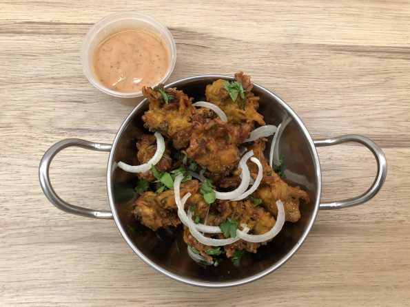 A serving bowl filled with vegetable pakora, beside a dipping pot of pink pakora sauce.
