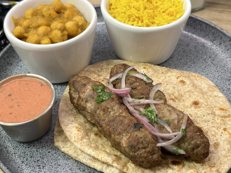 Lamb seekh kebab served on top of plain chapati with pink pakora sauce on the side.