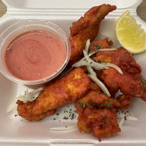 Chicken Pakora in a serving tray with sliced onion, coriander, a lemon wedge and pink pakora sauce.