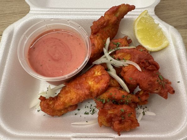 Chicken Pakora in a serving tray with sliced onion, coriander, a lemon wedge and pink pakora sauce.