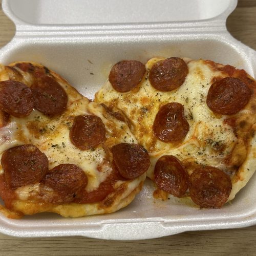 Naan pizza topped with pepperoni in a takeaway style container.