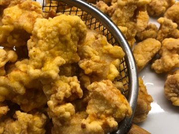 Cooked crispy chicken in a slotted spoon and on a serving plate.