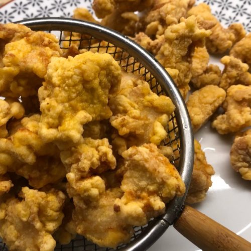 Cooked crispy chicken in a slotted spoon and on a serving plate.