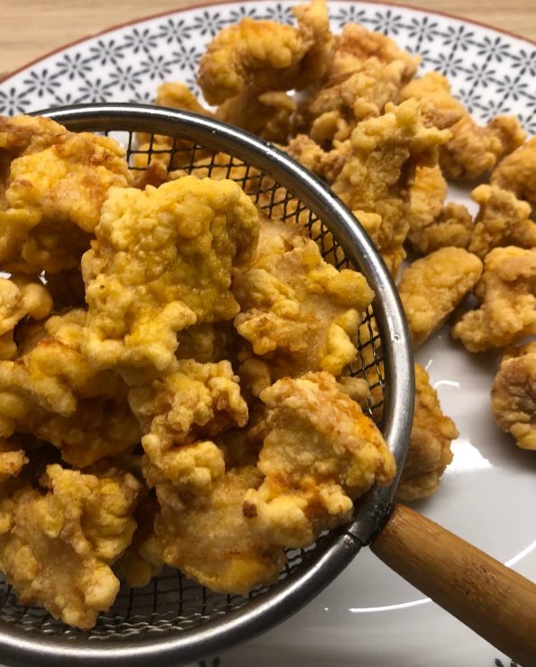 Cooked crispy chicken in a slotted spoon and on a serving plate.