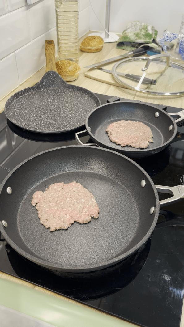 Minced beef meatballs smashed into burger patties in two frying pans.
