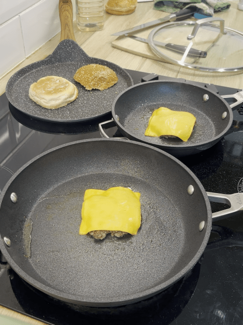 Smashed burgers topped with cheese, burger buns toasting.