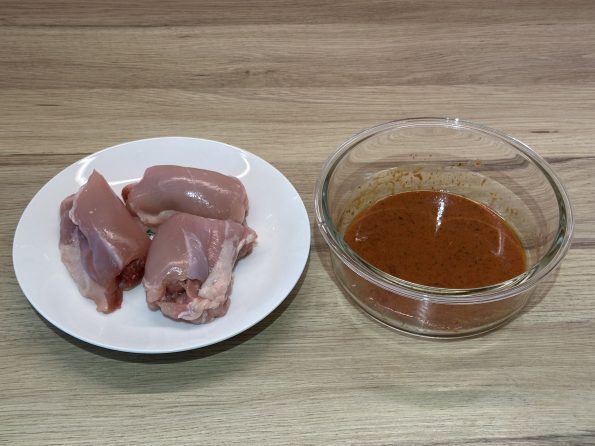 Skinless, boneless chicken thigh fillets beside a prepared bowl of tandoori style marinade.