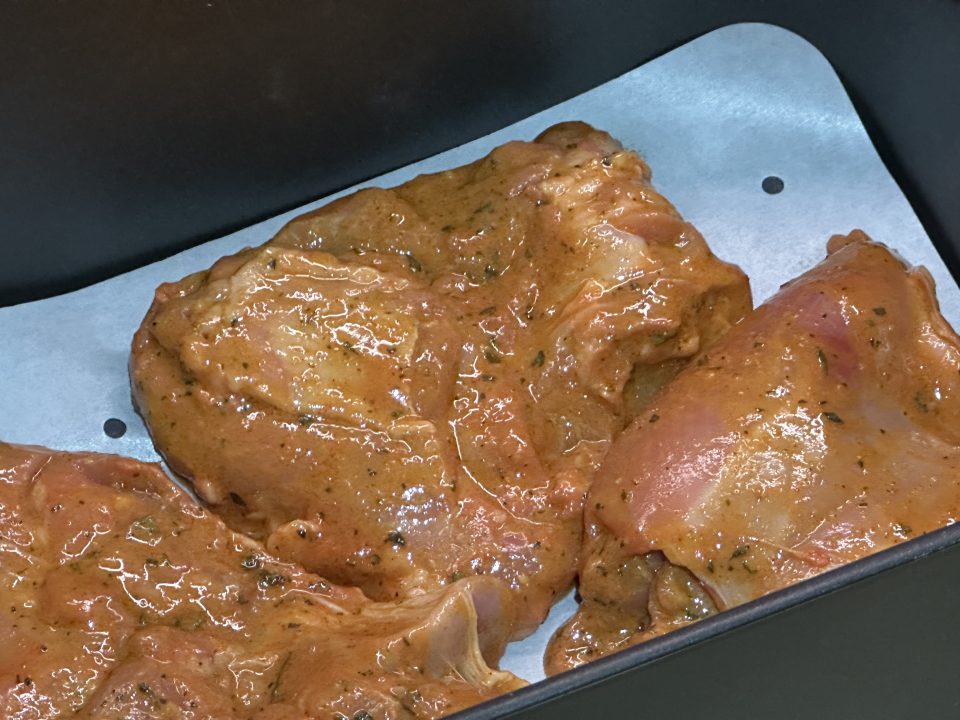 Marinated Indian takeaway style tandoori chicken thighs in an airfryer basket ready to cook.