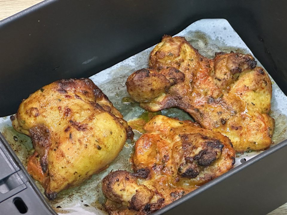 Cooked tandoori chicken thighs in an airfryer basket.