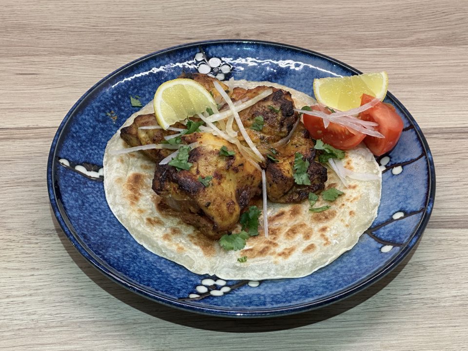 Indian takeaway style tandoori chicken thighs on top of a crispy paratha with sliced onion, fresh coriander, lemon wedges and tomatoes.