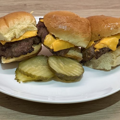 American fast food style cheeseburger sliders on a serving plate with sliced gherkins.
