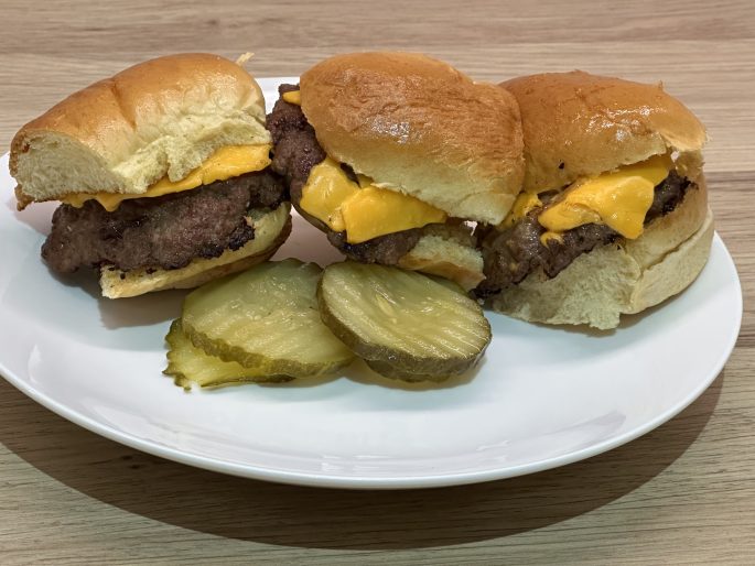 American fast food style cheeseburger sliders on a serving plate with sliced gherkins.