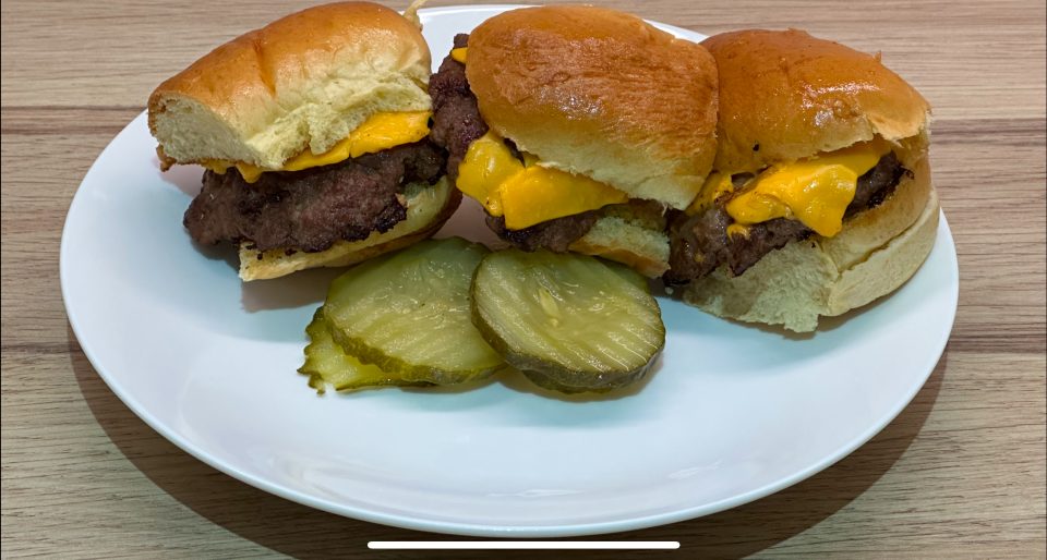 Cheeseburger sliders on a serving plate with sliced gherkins.