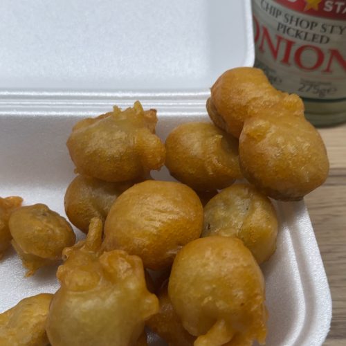 Chip shop style battered mushrooms in a serving tray beside a glass jar of pickled onions.