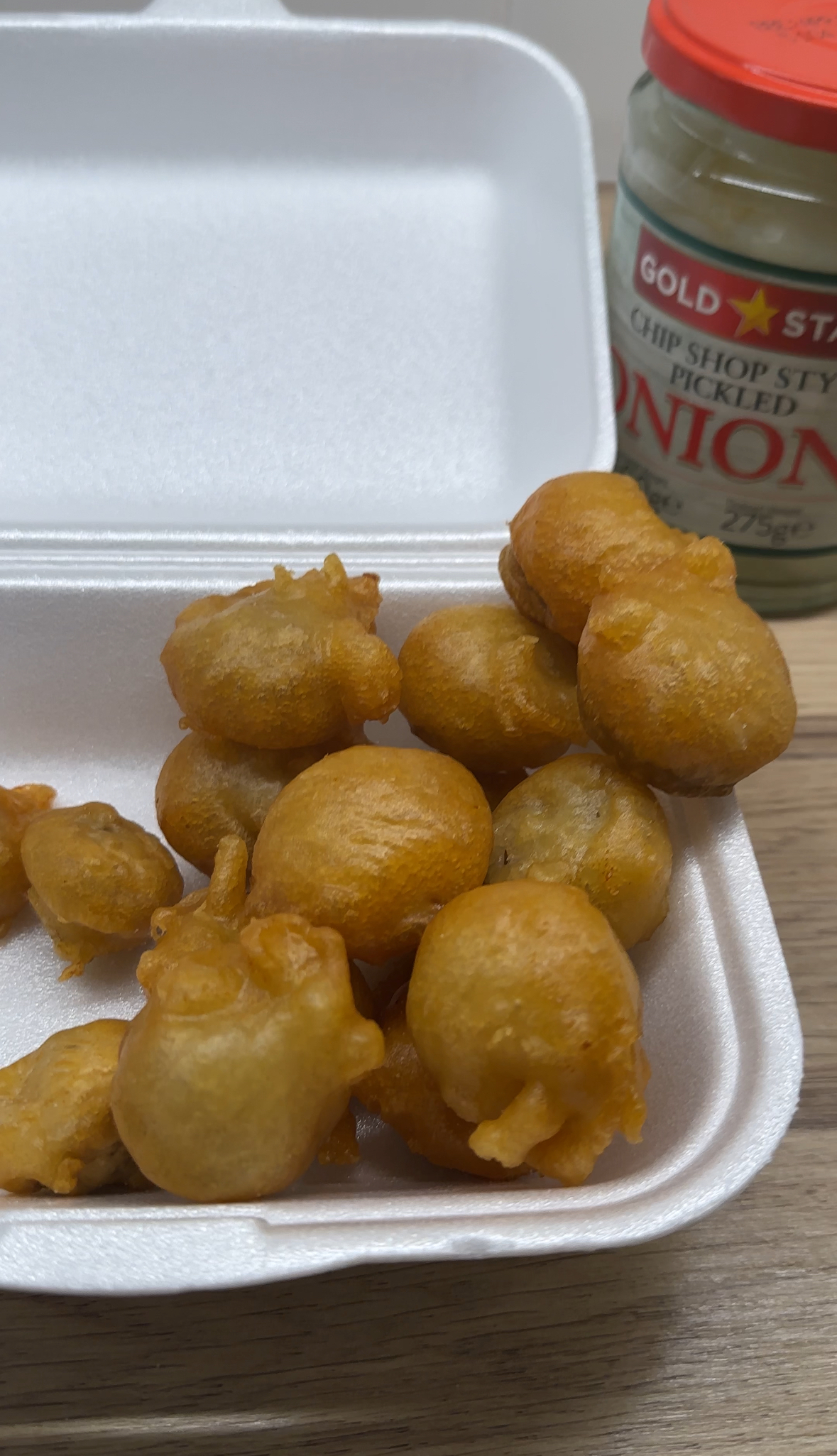 Chip shop style battered mushrooms in a serving tray beside a glass jar of pickled onions.